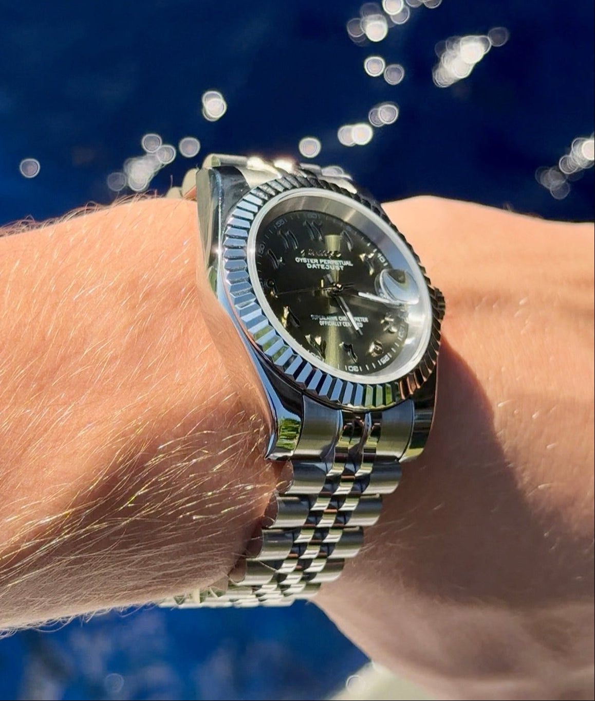 Close-up of a wrist wearing a silver watch with a blue water background